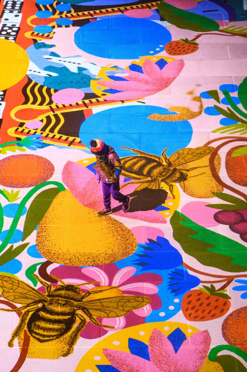 Child walking across multilcoloured floor projection with images of flowers, shapes, fruits and bees