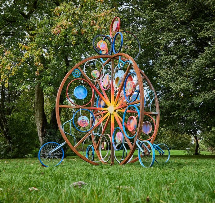 Khair in the community and Spencer Jenkins' installation. The structure is comprised of large interlocking metal circles with various hand drums and tambourines attached. Inspired by a traditional drum called the duf. The structure is covered in mandalas and has been spray painted in rich yellows, oranges and blues. Produced by Artichoke as part of Nuneaton & Bedworth Borough Council’s Creative Explorers programme. Photo by Andrew Moore