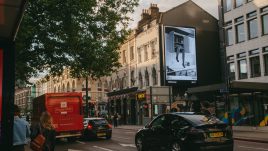 A busy city scene showing the artwork from The Gallery Season 4 on billboards. The artwork on display: A black-and-white image showing legs sticking out of a kitchen cupboard.