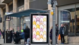 A busy city scene showing the artwork from The Gallery Season 4 on billboards. The artwork on display: A grid of tessellating sculptural tiles shaped like different sets of breasts