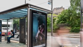 A busy city scene showing the artwork from The Gallery Season 4 on billboards. The artwork on display: A pregnant person in a pink bra gently cradling their belly.