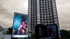 A busy city scene showing the artwork from The Gallery Season 4 on billboards. The artwork on display: A pregnant person in a pink bra gently cradling their belly.