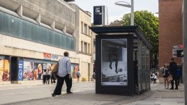 A busy city scene showing the artwork from The Gallery Season 4 on billboards. The artwork on display: A black-and-white image showing legs sticking out of a kitchen cupboard.