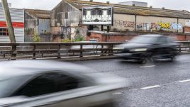 A busy city scene showing the artwork from The Gallery Season 4 on billboards. The artwork on display: A black-and-white image showing legs sticking out of a kitchen cupboard.